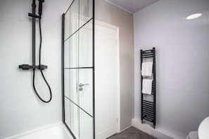 A modern bathroom with a glass shower enclosure, a white door, and a towel rack.