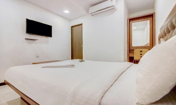 Une chambre à coucher comprenant un lit, un téléviseur à écran plat fixé au mur, un appareil de climatisation et une porte en bois.
