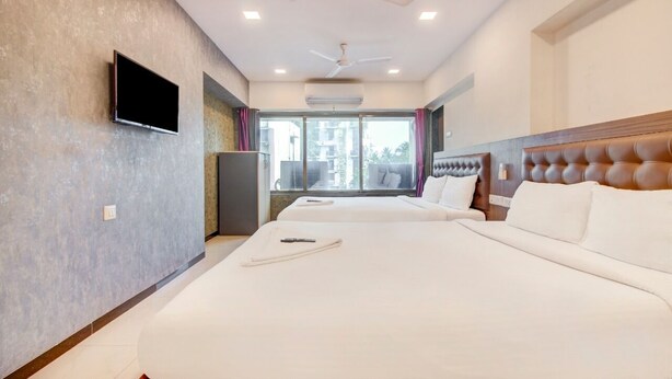Habitación de hotel con una cama grande, un televisor de pantalla plana en la pared, un ventilador de techo y un ventanal con cortinas.