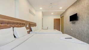 Habitación de hotel con dos camas, un televisor montado en la pared y un ventilador de techo.