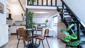 Une cuisine moderne avec des meubles blancs, un coin repas avec des chaises en bois et un escalier avec des rampes noires.