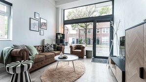 Un salon moderne avec un canapé en cuir marron, une table basse ronde et une grande fenêtre donnant sur un immeuble en briques.