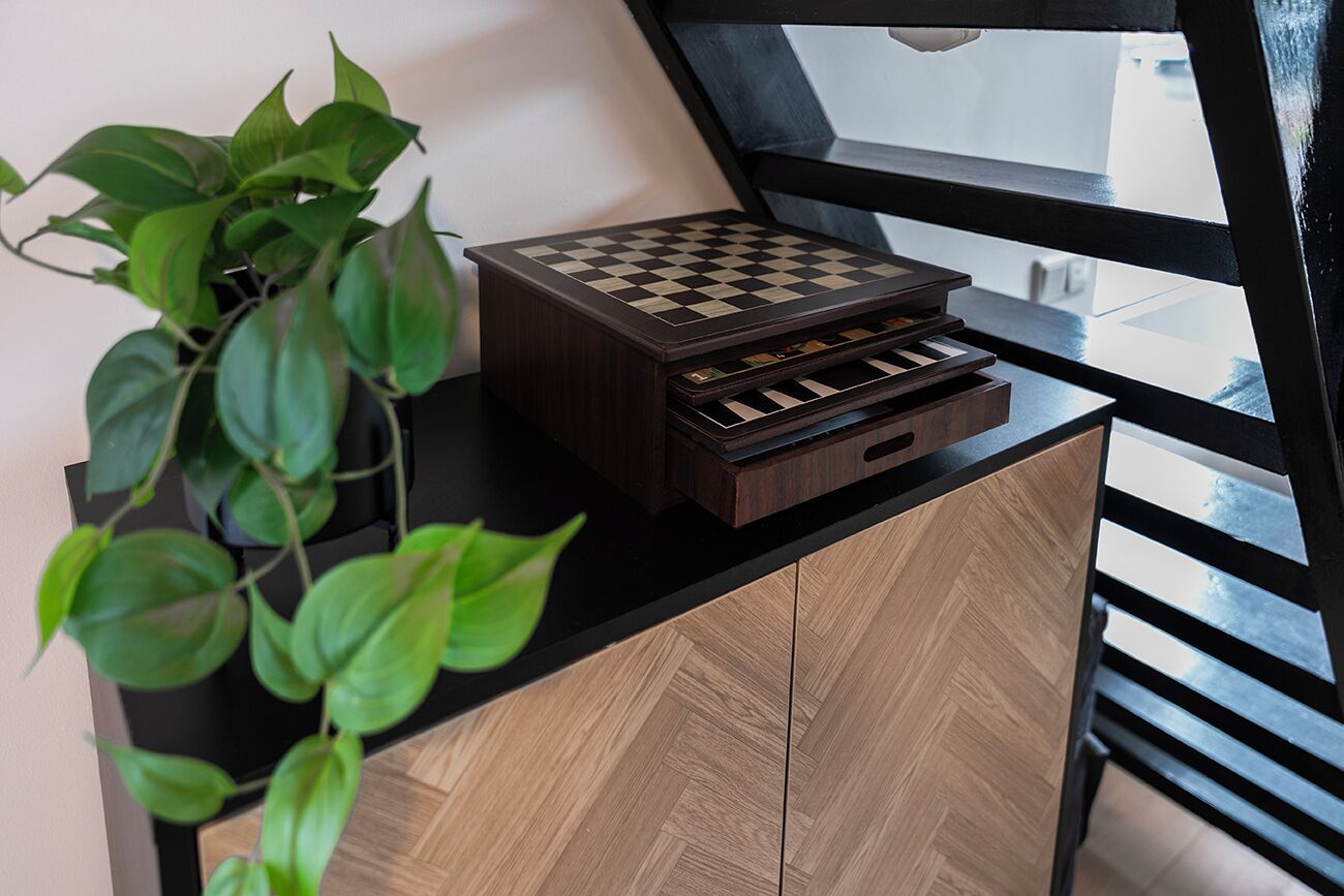 Una scacchiera su un mobile in legno con una pianta accanto.