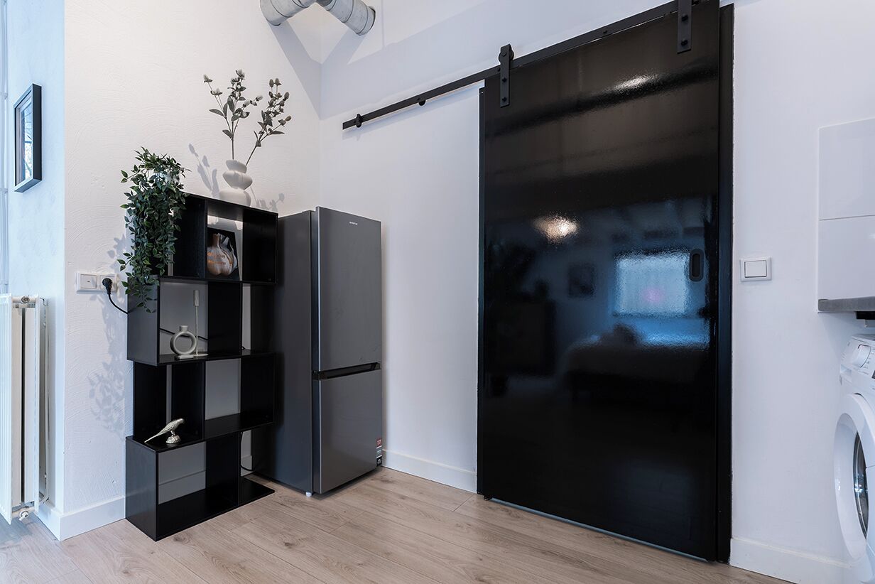 A modern kitchen with a black refrigerator, a black sliding door, and a white washing machine.