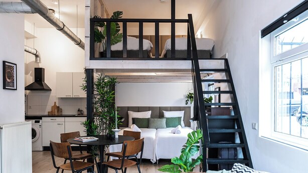 Un appartement compact comprenant une cuisine, un coin repas et une chambre en mezzanine accessible par un escalier.