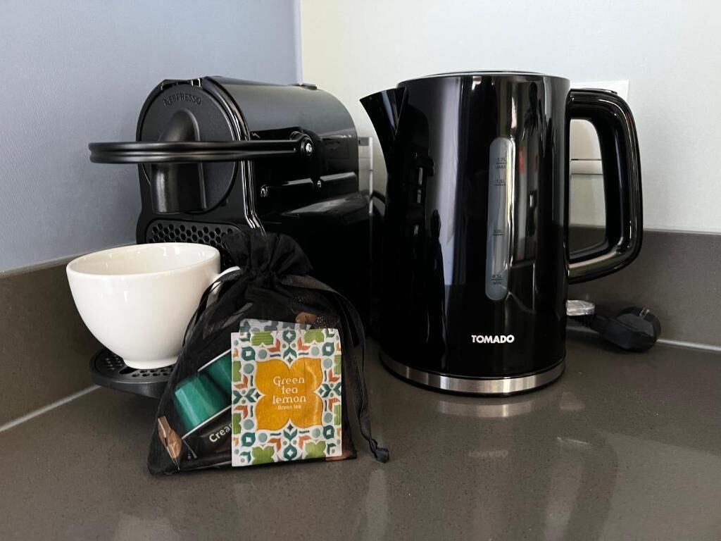 Ein Küchenbereich mit Kaffeemaschine, schwarzem Kaffee, einer weißen Tasse und einem Teebeutel.