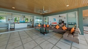 A spacious living area with a large sectional sofa, a glass coffee table, and a ceiling fan.