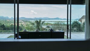 A room with a large window offering a view of a coastal landscape, including mountains and a body of water.