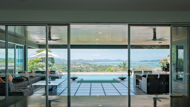 A modern living room with a large glass door leading to a pool area, offering a scenic view of the landscape.