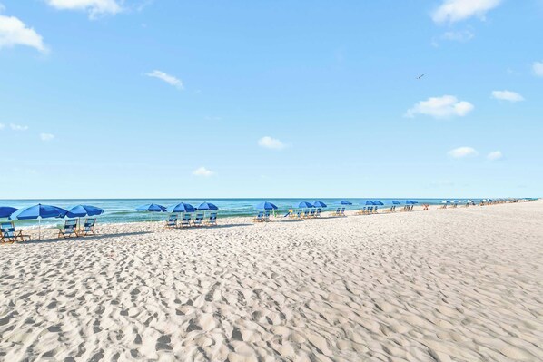 A beach with rows of blue umbrellas and lounge chairs.