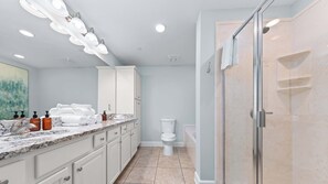 A modern bathroom with a marble countertop, white cabinets, a glass shower enclosure, and a toilet.