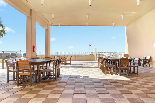 An outdoor patio with multiple tables and chairs, a tiled floor, and a view of the sea.
