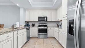 Une cuisine moderne avec des meubles blancs, des appareils en acier inoxydable et un plan de travail en granit.