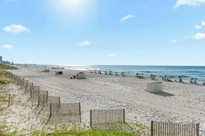 A wide sandy beach with a wooden fence, beach umbrellas, and a few beach huts.