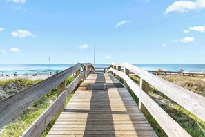 Une promenade en bois menant à une plage où l’on trouve des parasols et des chaises.