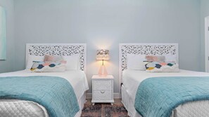 Une chambre avec deux lits, chacun doté d’une tête de lit blanche et recouvert d’un plaid à motifs. Une table de chevet avec une lampe se trouve entre les deux lits.