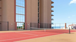 Ein Tennisplatz im Freien mit Netz, umgeben von einem Hochhaus mit großen Fenstern und Balkonen.