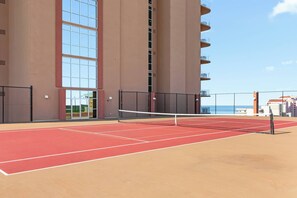 Ein Tennisplatz im Freien mit Netz, umgeben von einem Hochhaus mit großen Fenstern und Balkonen.