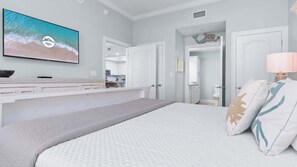 A bedroom with a large bed, a TV mounted on the wall, and a view of the bathroom through an open door. - Lazy River | 15th Floor Views | Beachfront Condo (Orange Beach)