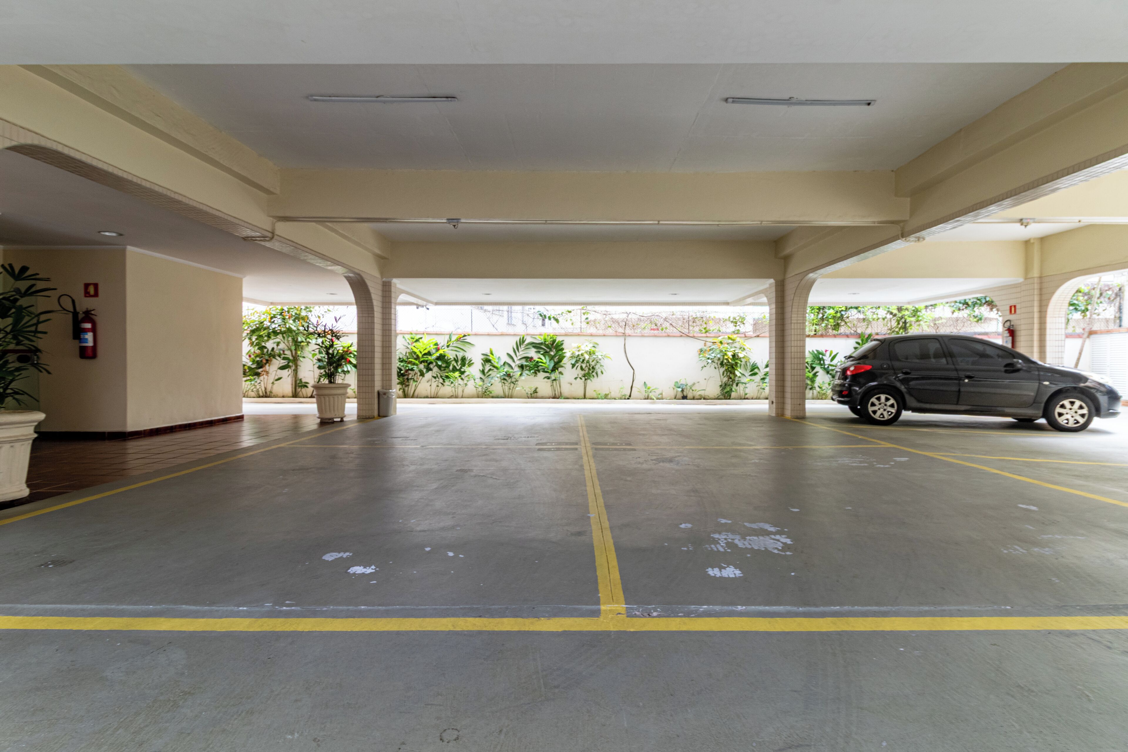 A covered parking area with a car parked, potted plants, and a fire extinguisher on the wall.