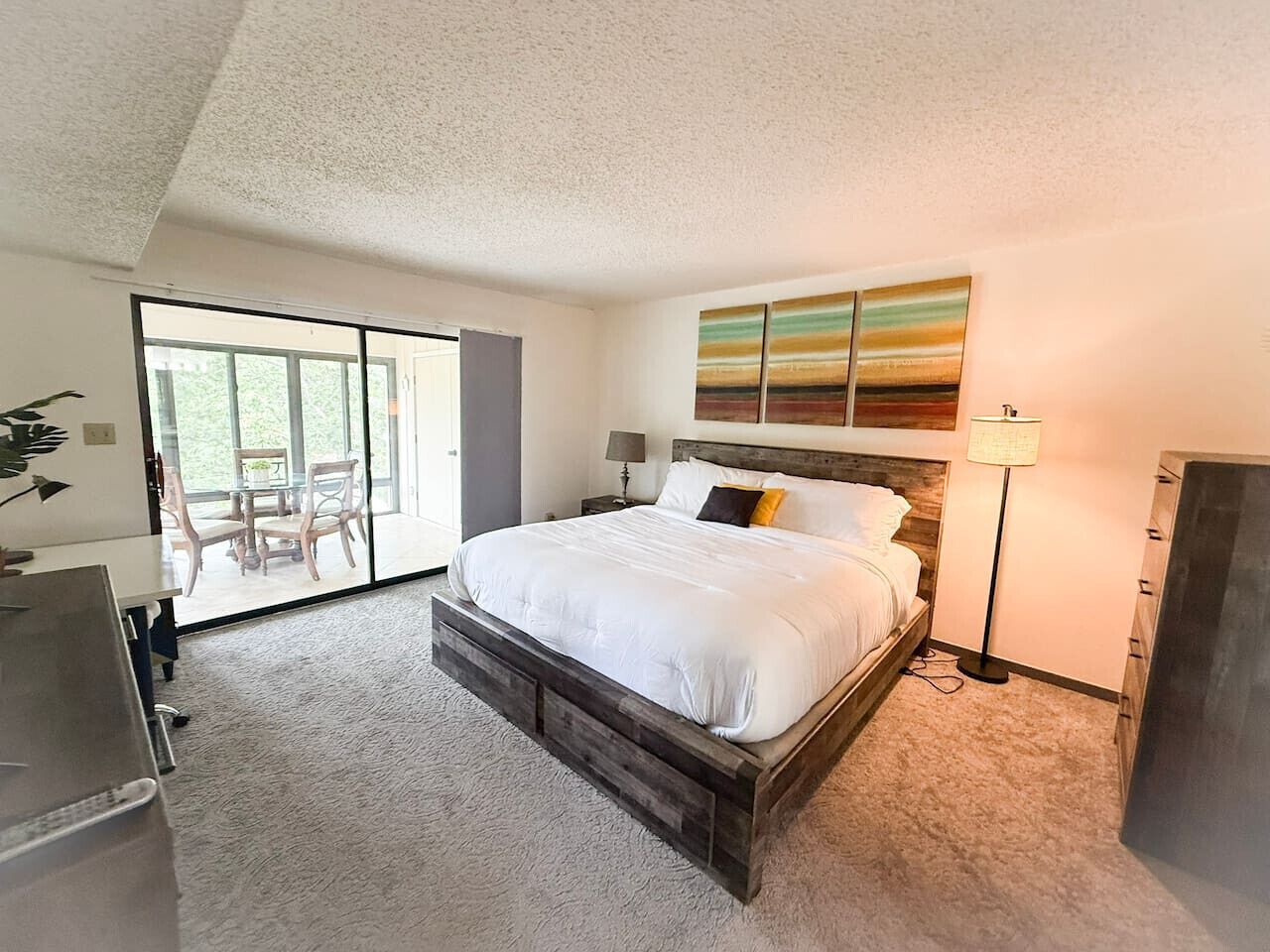 A bedroom with a large bed, a desk, a chair, and a view of a balcony.