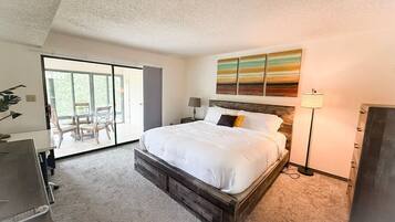 A bedroom with a large bed, a desk, a chair, and a view of a balcony.