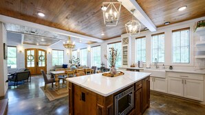 A spacious kitchen with a large island, wooden ceiling, and white cabinetry.