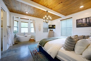 A bedroom with a wooden ceiling, a large bed, a bathtub, and a TV. - Sugarberry Farm | Farmhouse | hot tub | extra beds (Broken Bow)