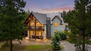 A two-story house with a stone facade, large windows, and a porch with outdoor seating.