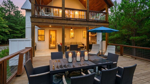 A two-story wooden house with a deck, outdoor seating, and a large dining table.
