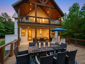 A two-story wooden house with a deck, outdoor seating, and a large dining table. - Sugarberry Farm | Farmhouse | hot tub | extra beds (Broken Bow)