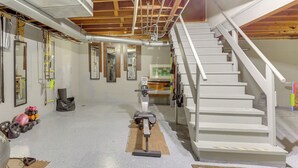 Un gimnasio en casa con equipo de ejercicio, una escalera y tuberías del techo a la vista.