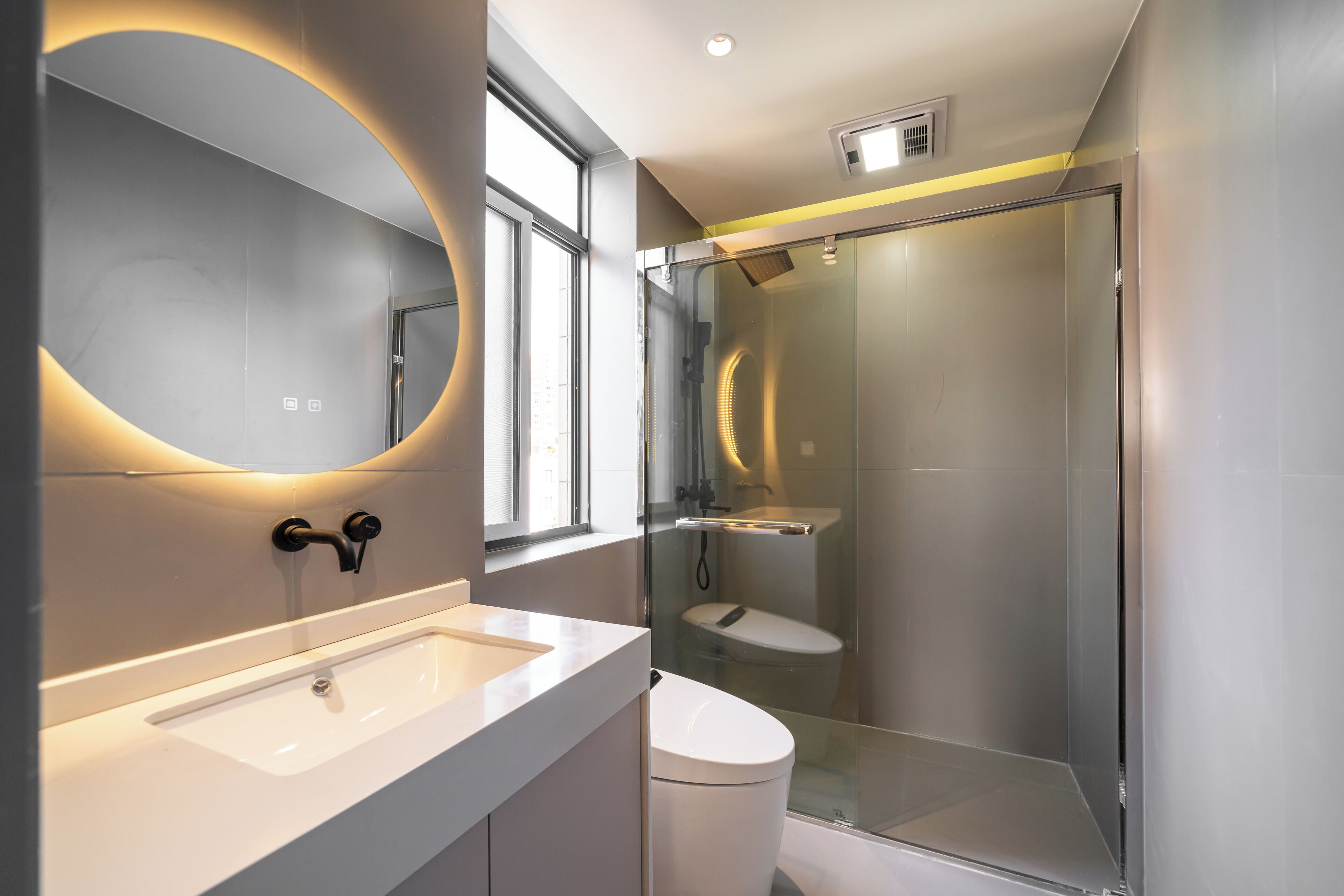 A modern bathroom with a glass-enclosed shower, a white sink, and a large mirror with a circular light.