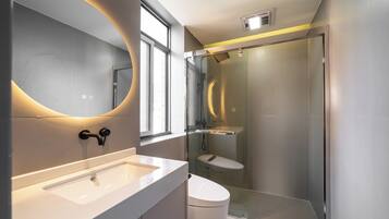 A modern bathroom with a glass-enclosed shower, a white sink, and a large mirror with a circular light.
