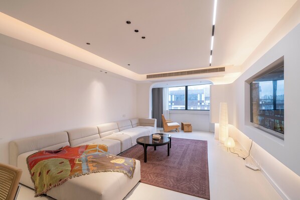 A modern living room with a sofa, armchair, and coffee table, a large window with a view, and a ceiling light fixture.