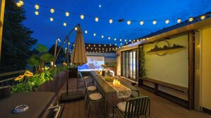 An outdoor deck with string lights, a long table, chairs, and a projector screen. - Book and Bed - Xujiahui (Shanghai)