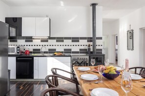 A modern kitchen with a dining area, featuring a wooden table set for a meal, a black stove, and a microwave. - Holiday Home With Pool Near Makarsk (Proložac)
