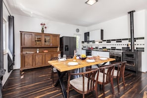 A modern kitchen with a dining area, featuring a wooden cabinet, a refrigerator, a stove, and a dining table set for four. - Holiday Home With Pool Near Makarsk (Proložac)