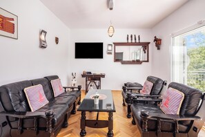 A modern living room with leather sofas, a glass coffee table, and a flat-screen TV mounted on the wall.