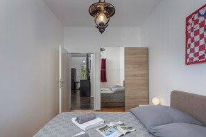 Quarto com cama, um espaço de leitura com revista, painel de madeira e um objeto xadrez vermelho na parede.