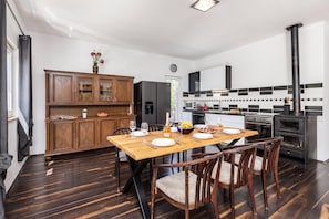 A modern kitchen with a dining area, featuring a wooden cabinet, a refrigerator, a stove, and a dining table set for four. - Holiday Home With Pool Near Makarsk (Proložac)