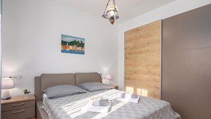 A modern bedroom with a bed, bedside tables, a nightstand, a lamp, a painting, and a wooden panel on the wall. - Holiday Home With Pool Near Makarsk (Proložac)