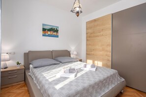A modern bedroom with a bed, bedside tables, a nightstand, a lamp, a painting, and a wooden panel on the wall. - Holiday Home With Pool Near Makarsk (Proložac)