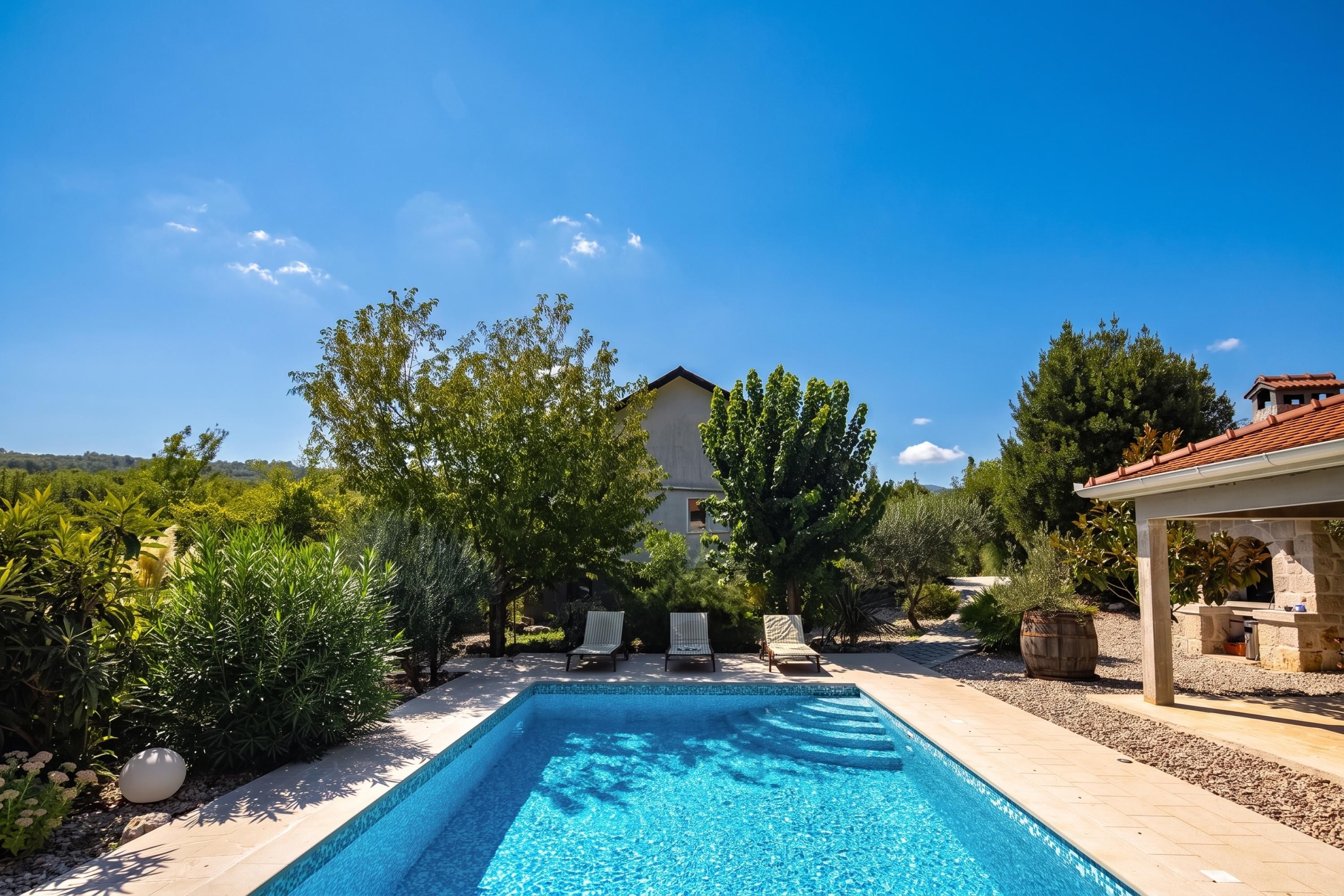 A swimming pool with a clear blue water, surrounded by trees and a building in the background.