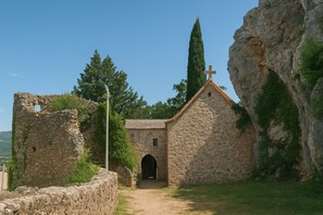 Eine steinerne Kirche mit Kruzifix, umgeben von viel Grün und blauem Himmel.