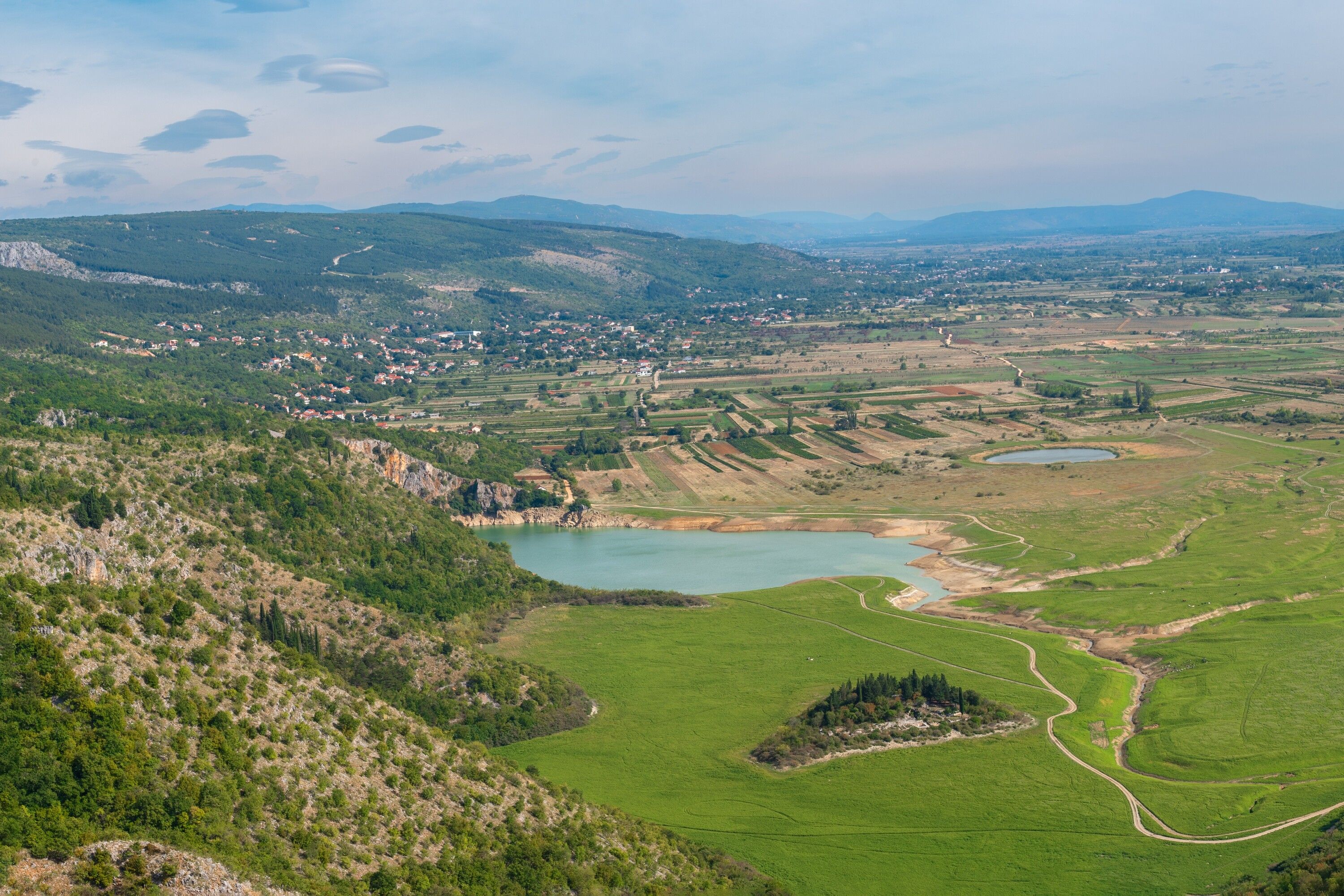 A panoramic view of a rural landscape with a small town, green fields, and a lake.