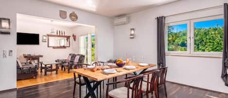 A dining area with a wooden table, chairs, and a view of greenery through the window.