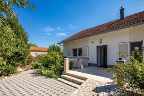A two-story house with a tiled roof, a front porch, and a garden with various plants and a small statue. - Holiday Home With Pool Near Makarsk (Proložac)