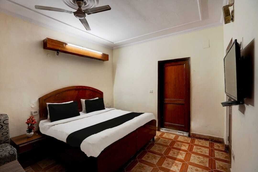 A hotel room with a bed, a ceiling fan, a TV, and a door.