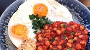 Un plato con dos huevos estrellados, una porción de garbanzos en salsa de tomate y un trozo de pan.